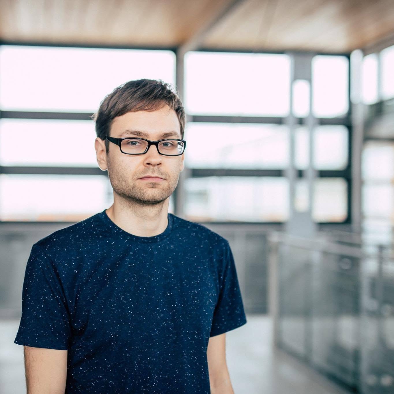 Portrait of Robert Reimer, standing indoors in front of large windows.