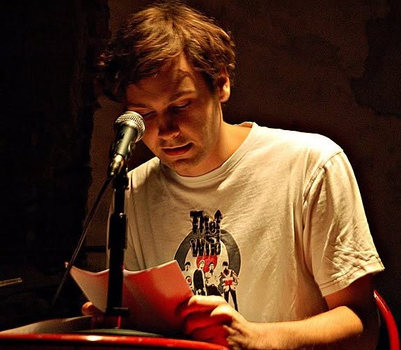 Robert Reimer reading fiction aloud at a microphone.